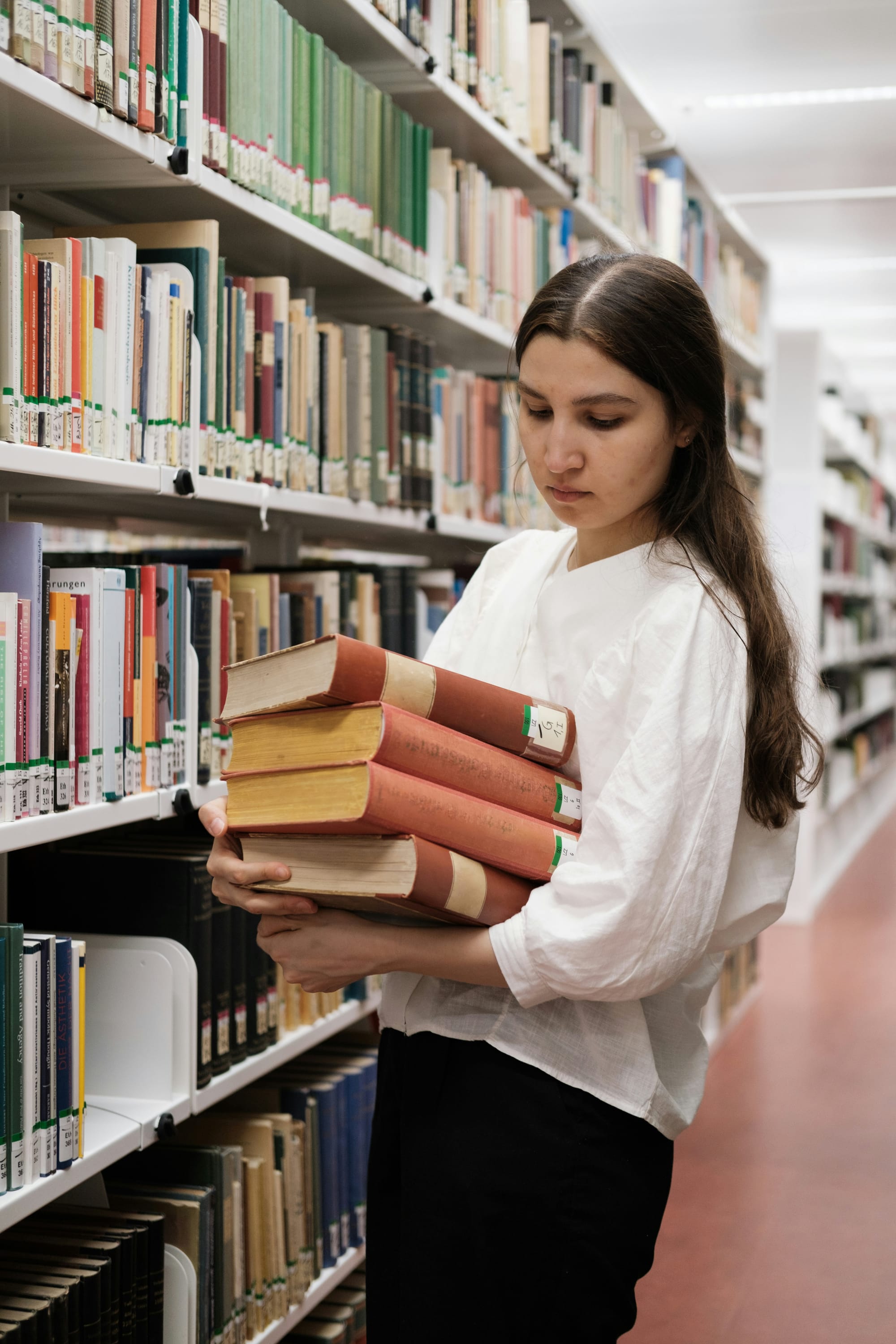 A woman carrying a stack of books in a library