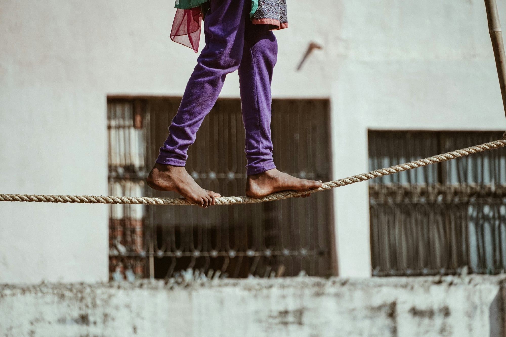 Bare feet balancing on a rope against a weathered urban backdrop