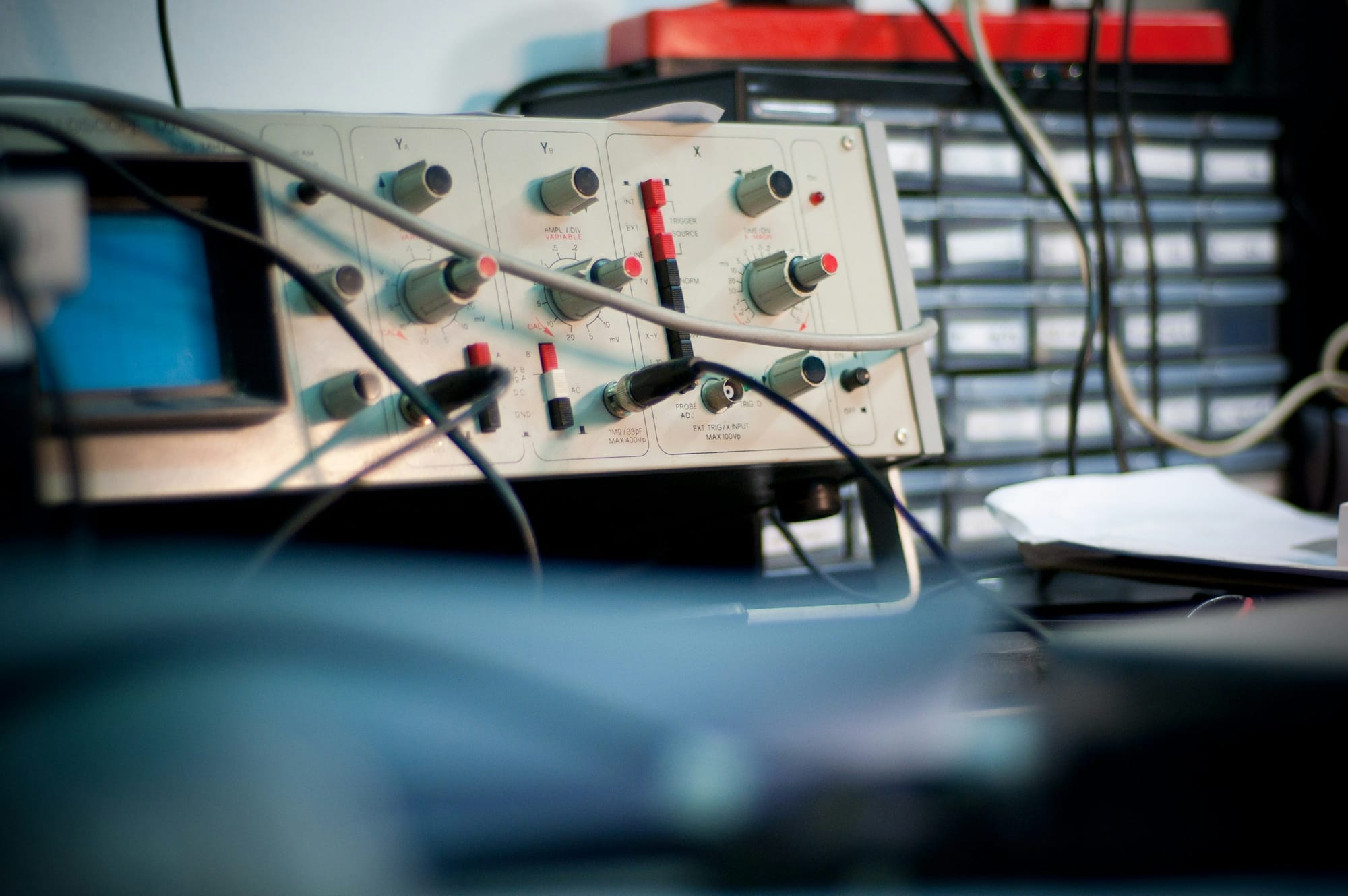 A vintage oscilloscope on a desk with cables running out of frame, knobs in the foreground