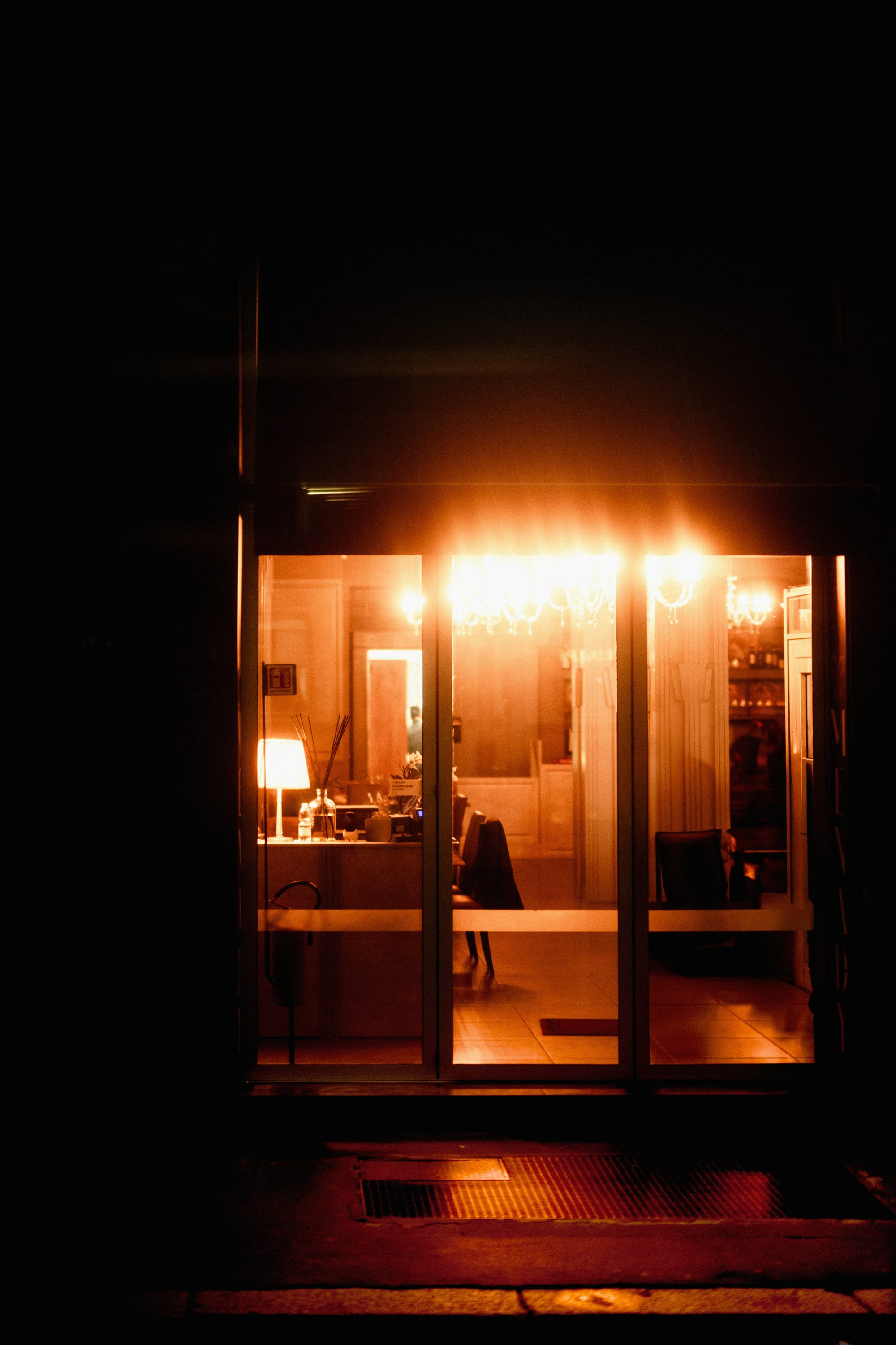 A warm, lit room glimpsed from the dark street outside at night