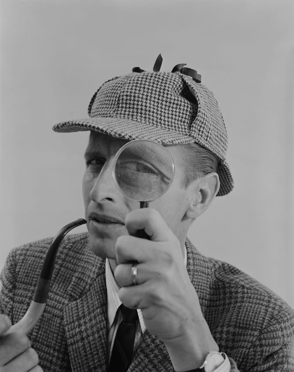 A man in a deerstalker hat looking through a magnifying glass, Sherlock Holmes style